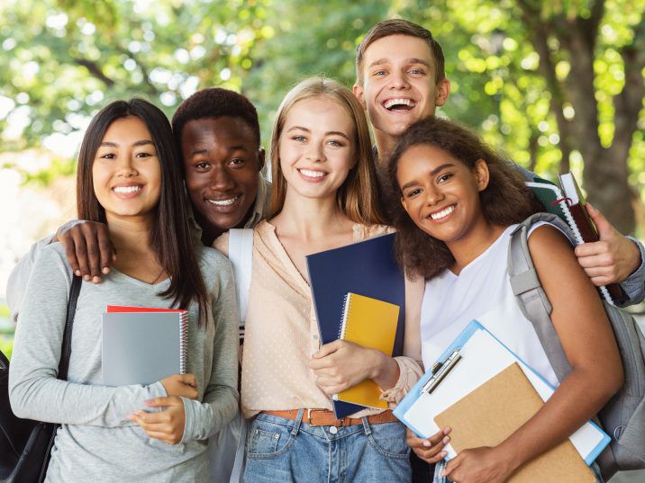 Group of smiling high school students holding notebooks outdoors